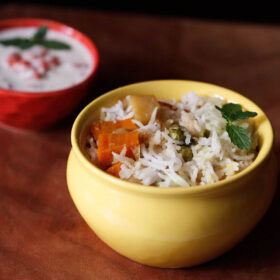 vegetable biryani served in a ceramic yellow handi with a bowl of raita on the side.