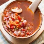 top shot of vegetable soup in a cream colored ceramic mug with a ceramic spoon inside the bowl.