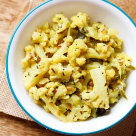 cauliflower poriyal in an aqua color rimmed white bowl on burlap.