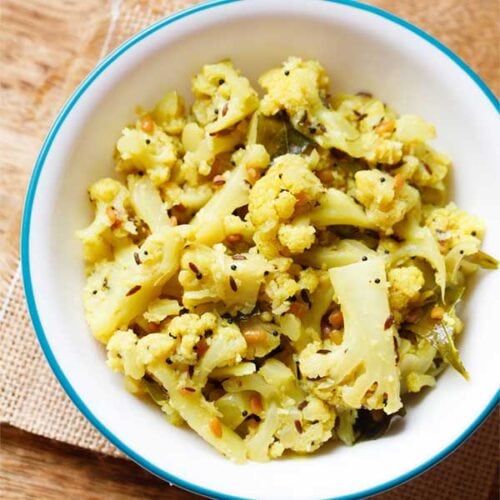 cauliflower poriyal in an aqua color rimmed white bowl on burlap.