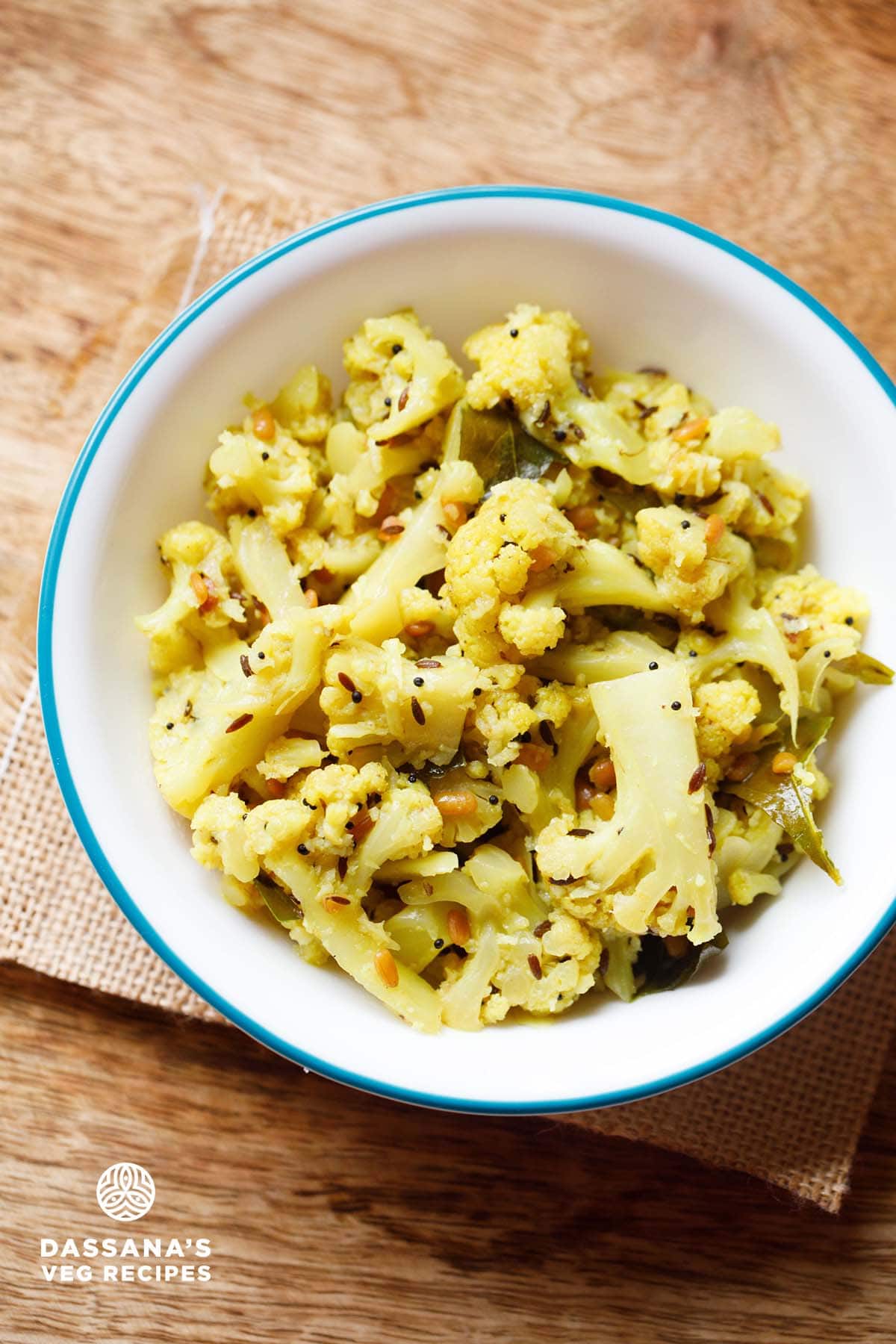 cauliflower poriyal in an aqua color rimmed white bowl on burlap.