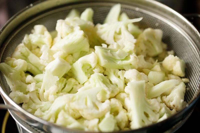 blanched cauliflower florets being strained in a strainer.