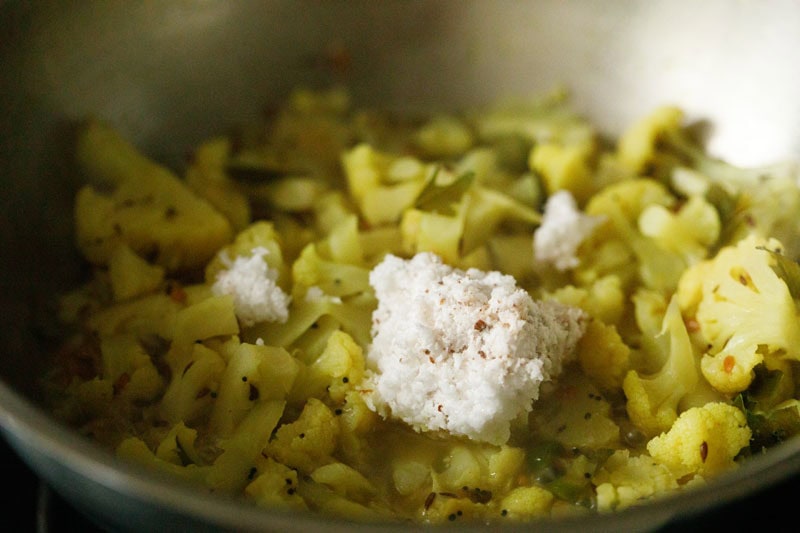 grated coconut on top of the almost cooked cauliflower florets in pan.