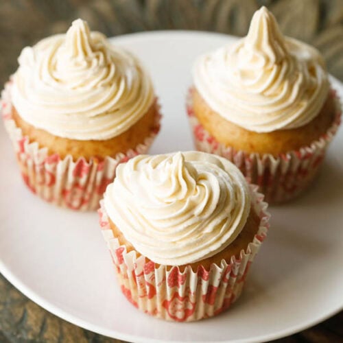 three buttercream frosted eggless cupcakes on a white plate in red and white cupcake liners.