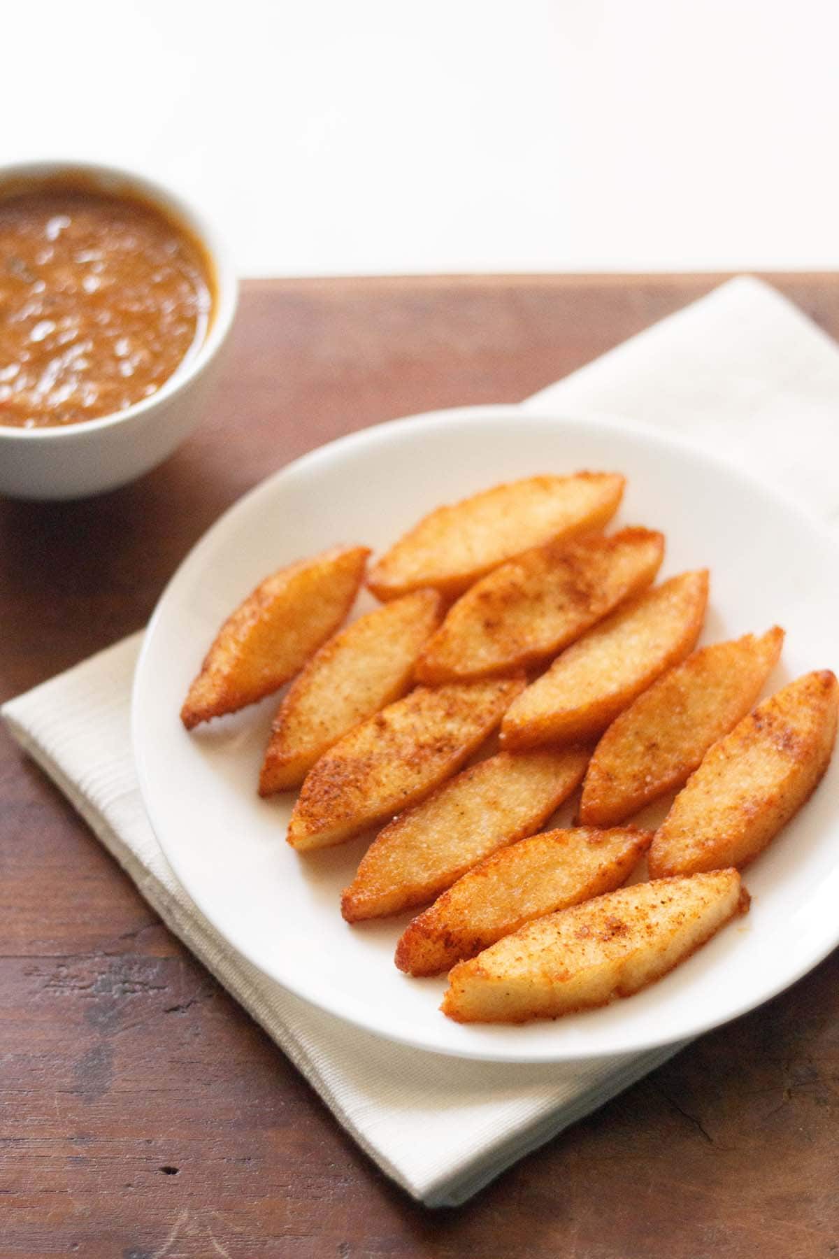 fried idli served on a white plate with a bowl of tomato chutney kept on the top left side. 