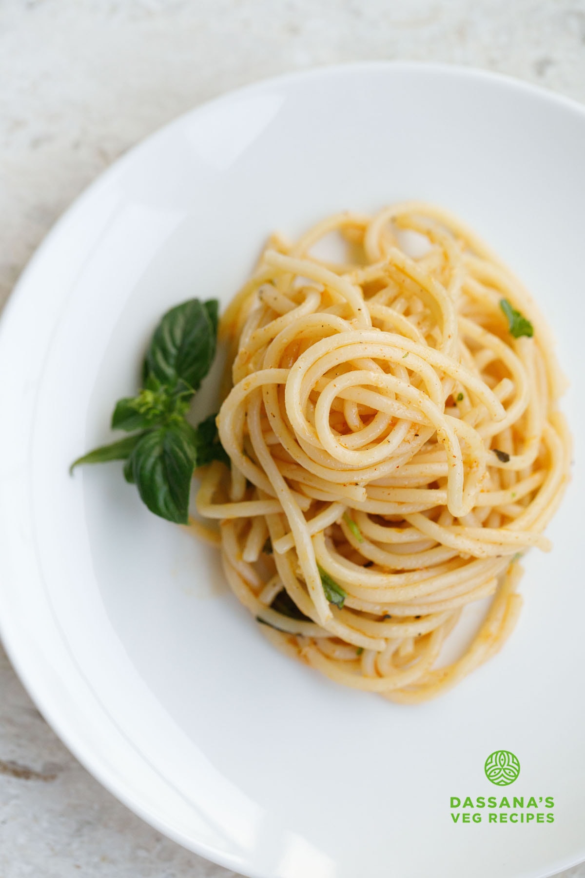 garlic pasta served on a white plate with a basil sprig by the side.