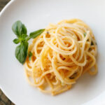 garlic butter pasta on a white plate with a basil sprig by the side.