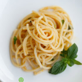 garlic butter pasta served on a white plate with a basil sprig by the side.