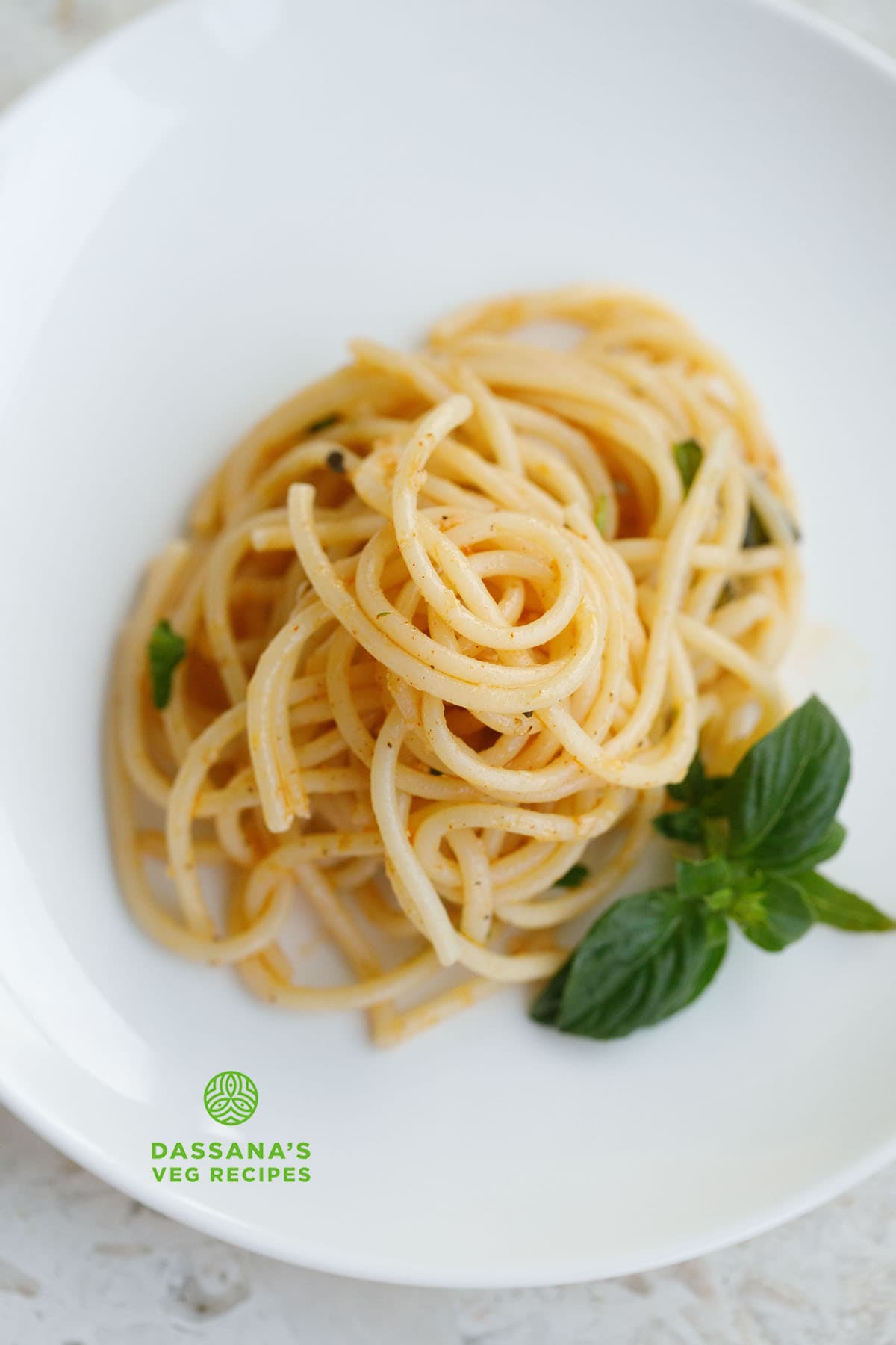 garlic butter pasta served on a white plate with a basil sprig by the side.