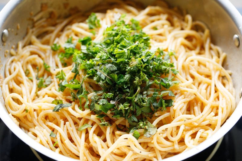 chopped herbs on garlic butter pasta in pan.