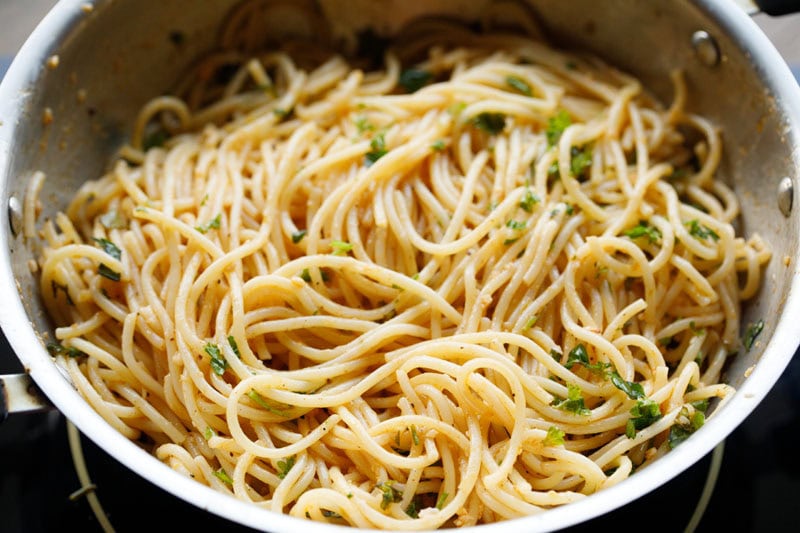 spaghetti mixed with herbs in pan.