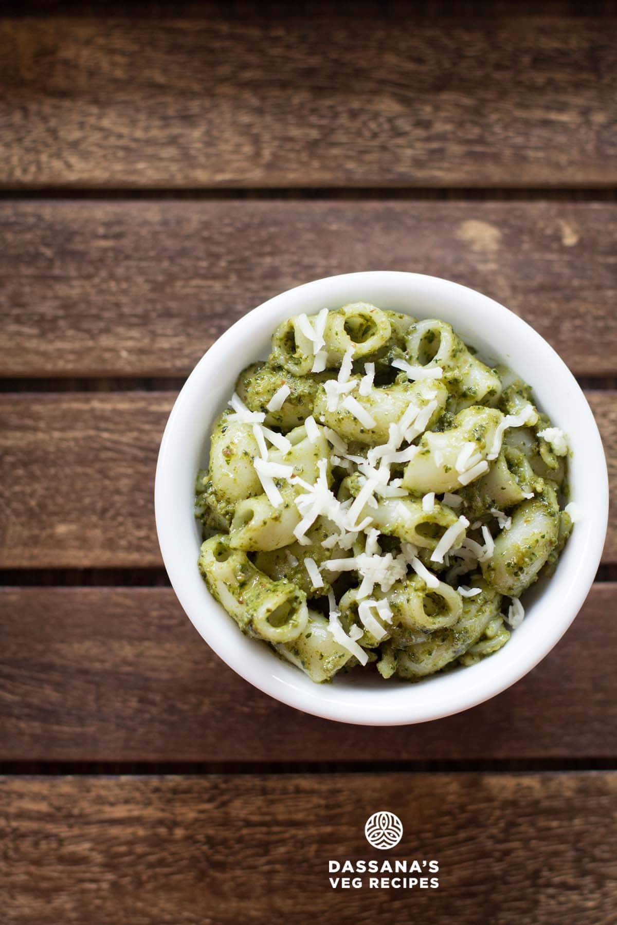 pesto pasta served in a white bowl topped with some grated parmesan on a dark brown wooden tray