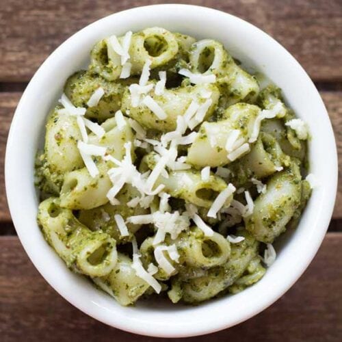 pesto pasta served in a white bowl topped with some grated parmesan.