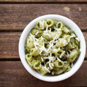 pesto pasta served in a white bowl topped with some grated parmesan on a dark brown wooden tray with text layovers.