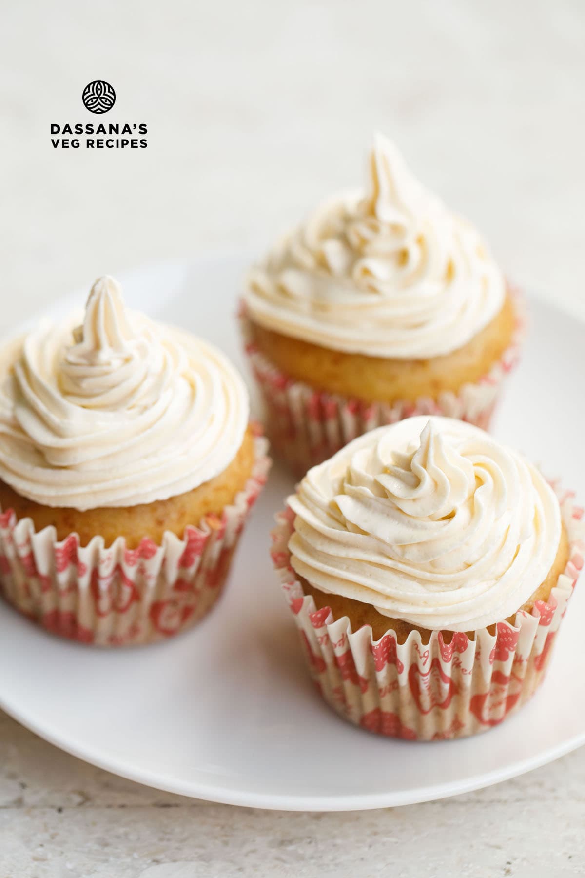 three vanilla cupcakes frosted with buttercream icing on a white plate with text layovers.