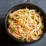 veg noodles served in a black bowl on a dark blue-gray wooden board.