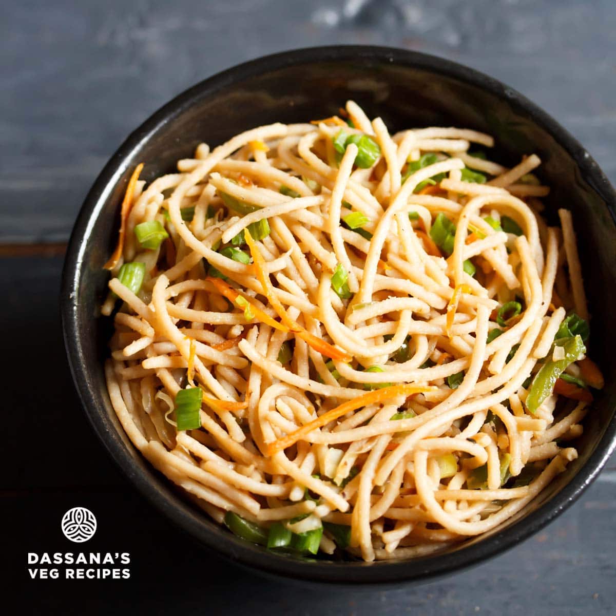 vegetable noodles served in a black bowl on a dark blue-gray wooden board.