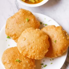 bedmi puri on white plate with chana aloo gravy (sabzi) placed on top in a white bowl.