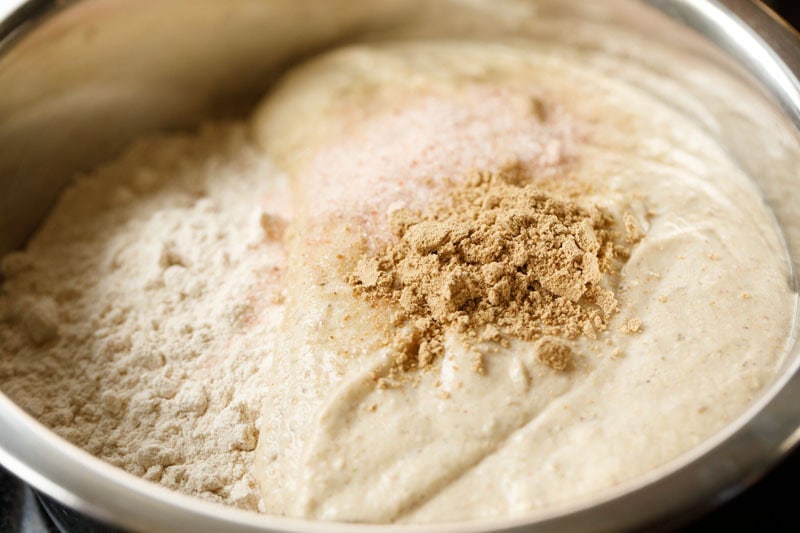 urad dal paste, salt, dried mango powder on top of whole wheat flour in mixing bowl.