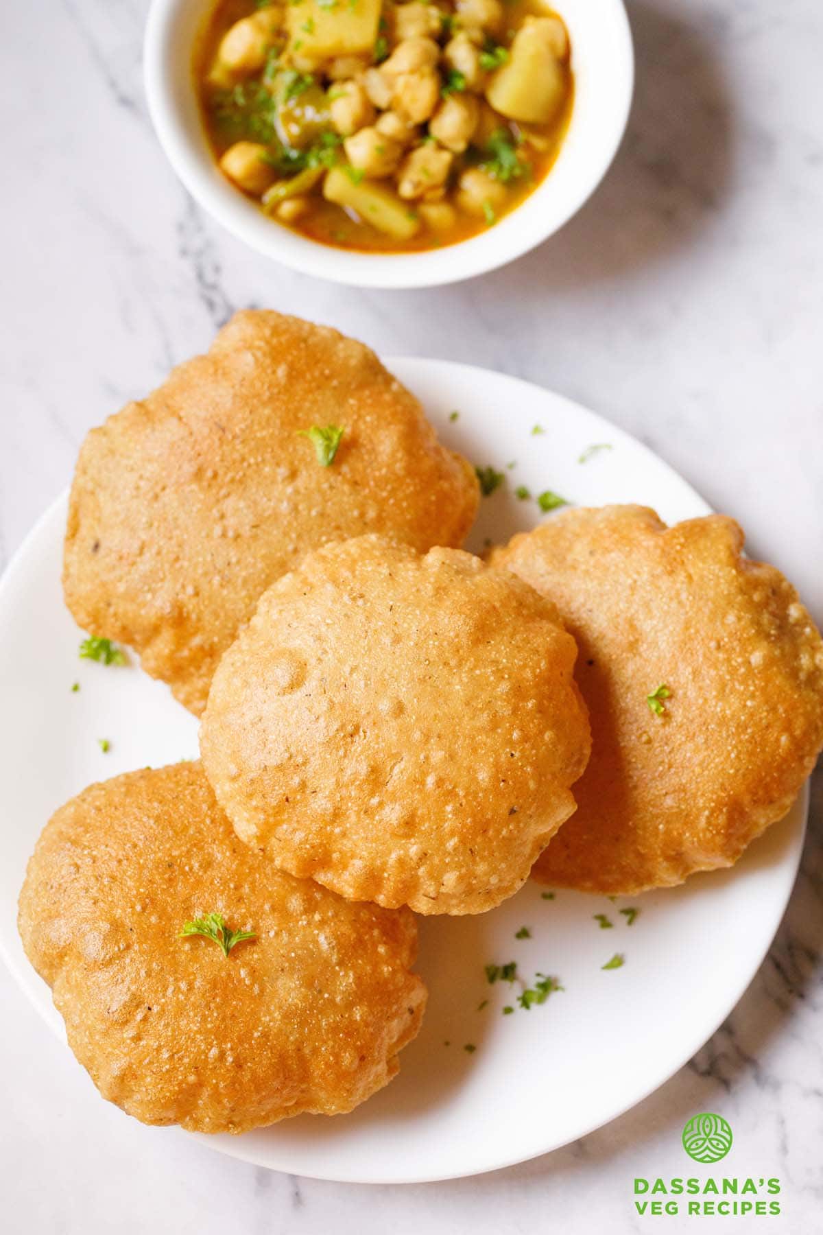 bedmi puri on white plate with chana aloo gravy (sabzi) placed on top in a white bowl.