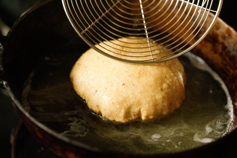 bedmi puri being nudged with a frying spoon to help it puff.