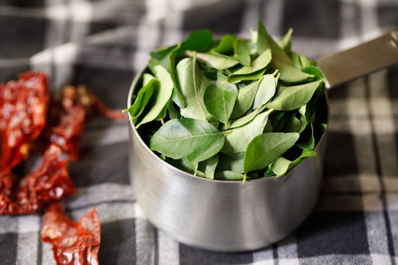 plucked curry leaves in a steel measuring cup.