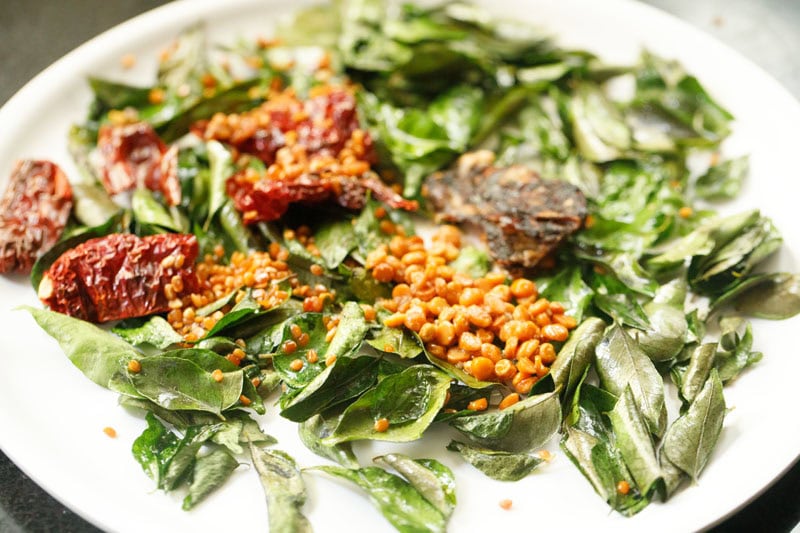 roasted ingredients to make curry leaves powder cooling on a white plate.