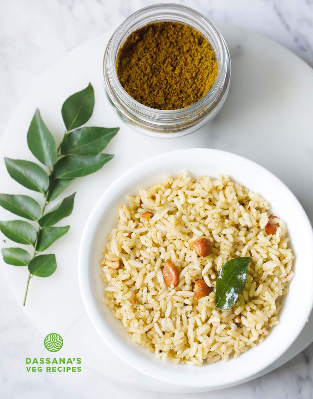 curry leaves rice on a white plate with karivepaku podi in a jar and curry leaves sprig on the side.