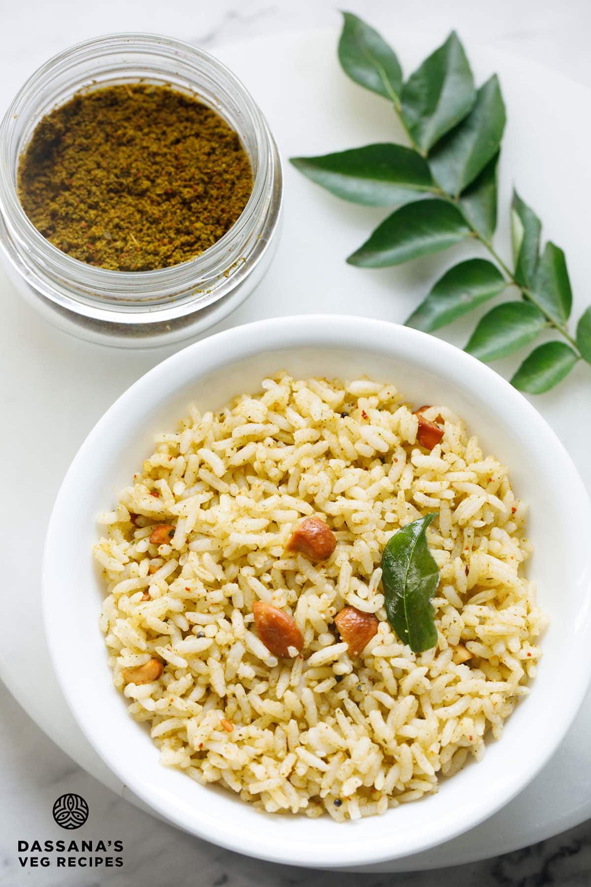 curry leaves rice on a white plate with curry leaves powder in a jar and curry leaves sprig on the side.