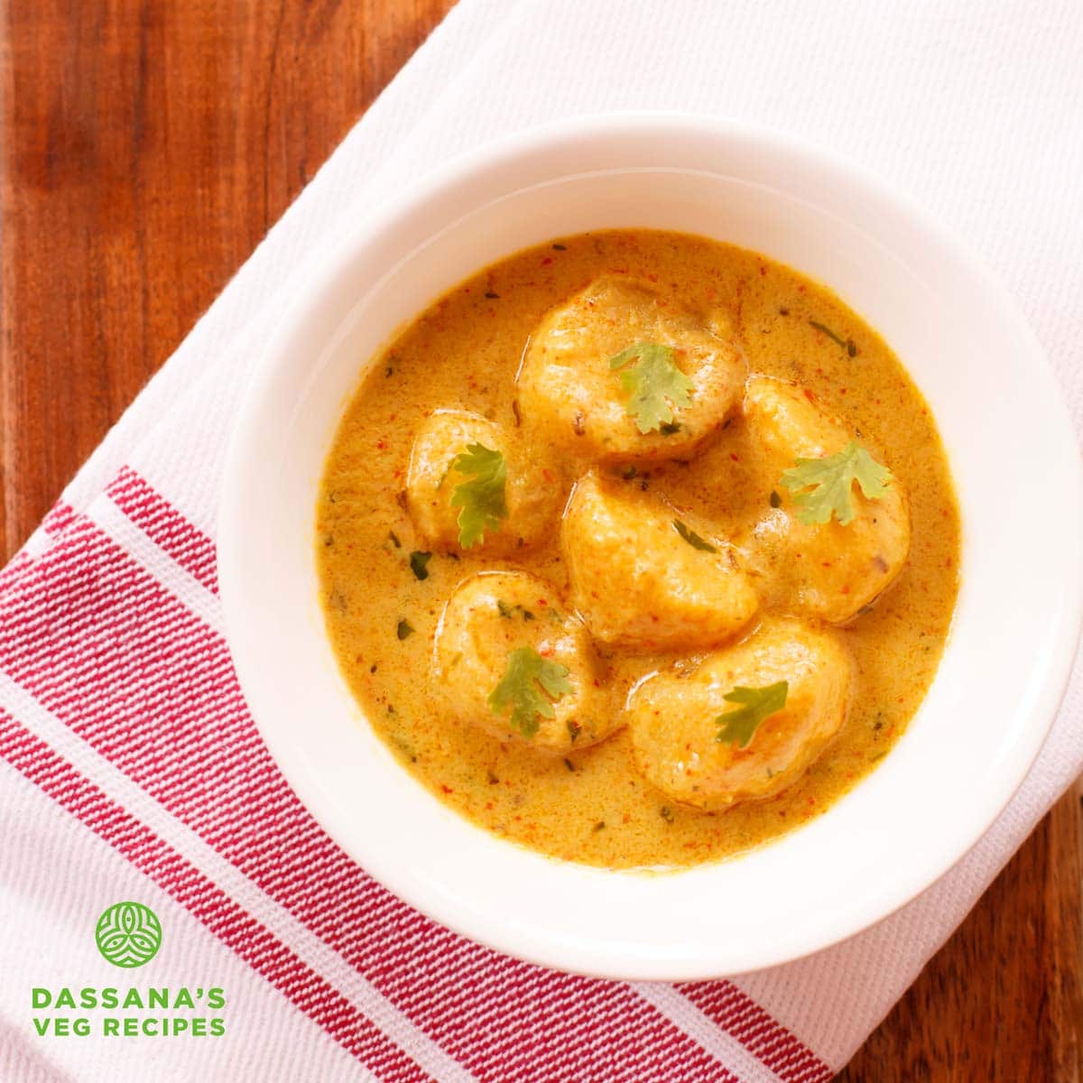 restaurant style dum aloo garnished with coriander leaves and served in a white bowl.