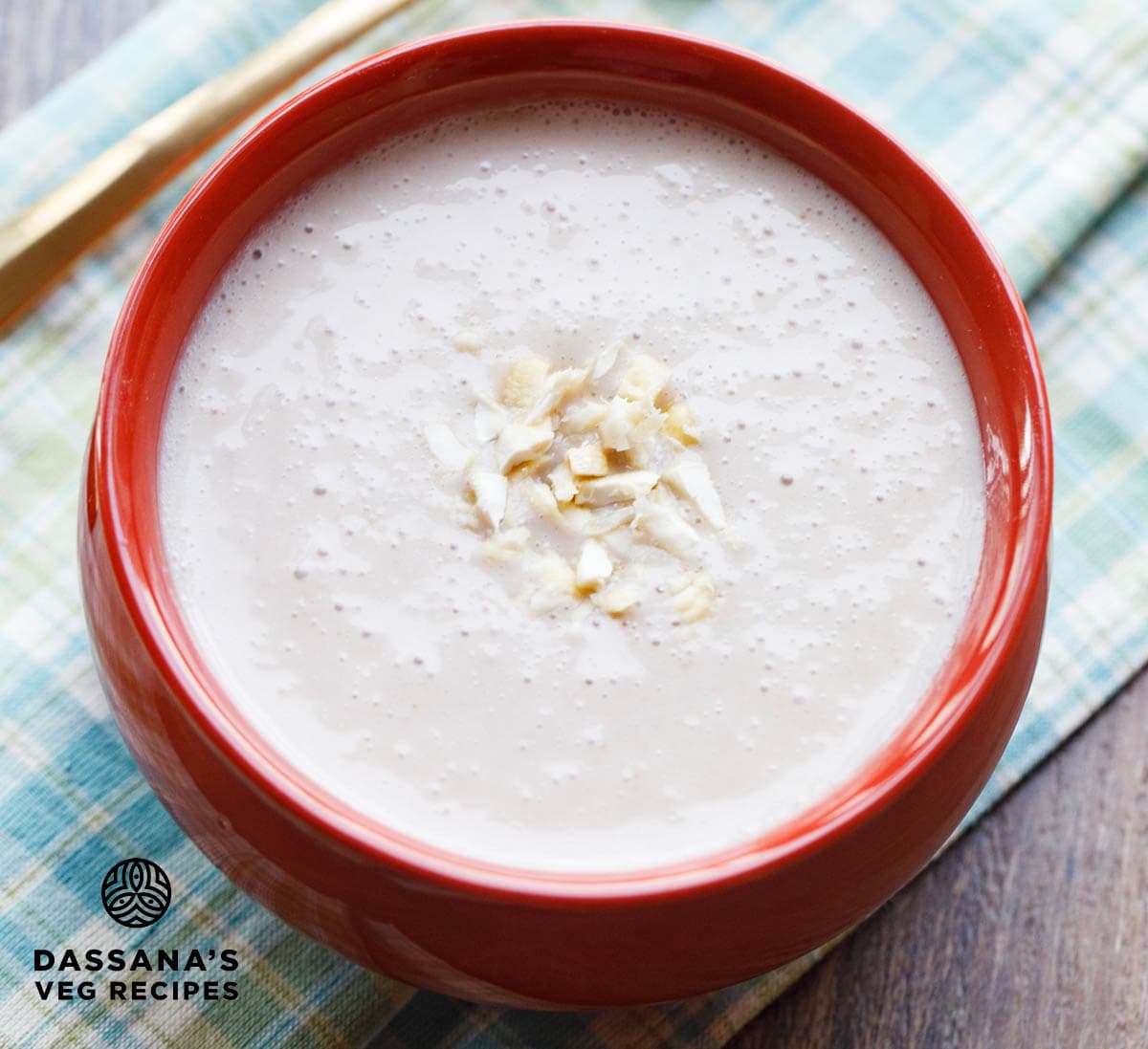 elaneer payasam in rust colored bowl topped with chopped cashews on a green blue colored checkered napkin.