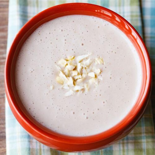 elaneer payasam in rust colored bowl topped with chopped cashews on a green blue colored checkered napkin.