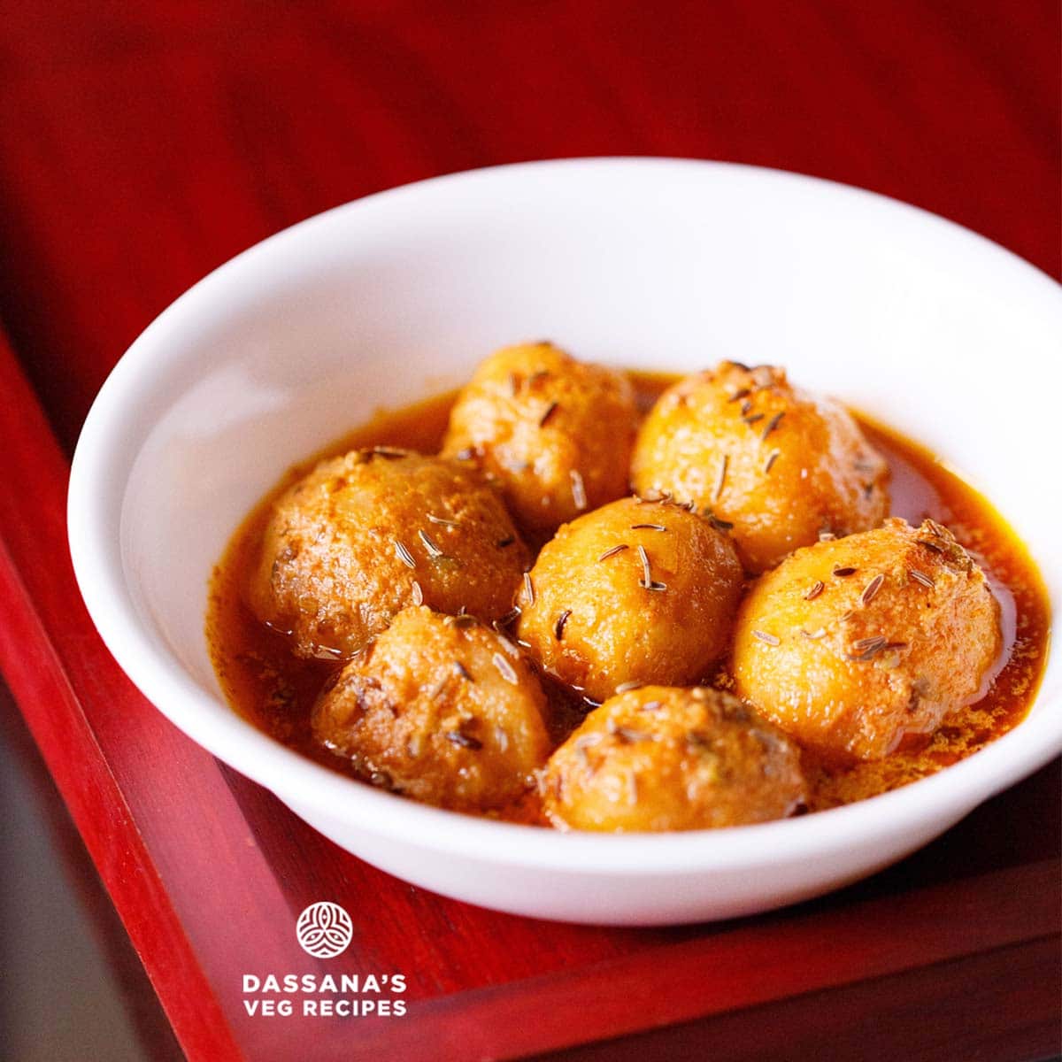 kashmiri dum aloo served in a white bowl on a red wood tray.