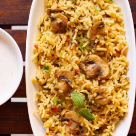 overhead shot of mushroom biryani in an oblong white tray on a wooden board.