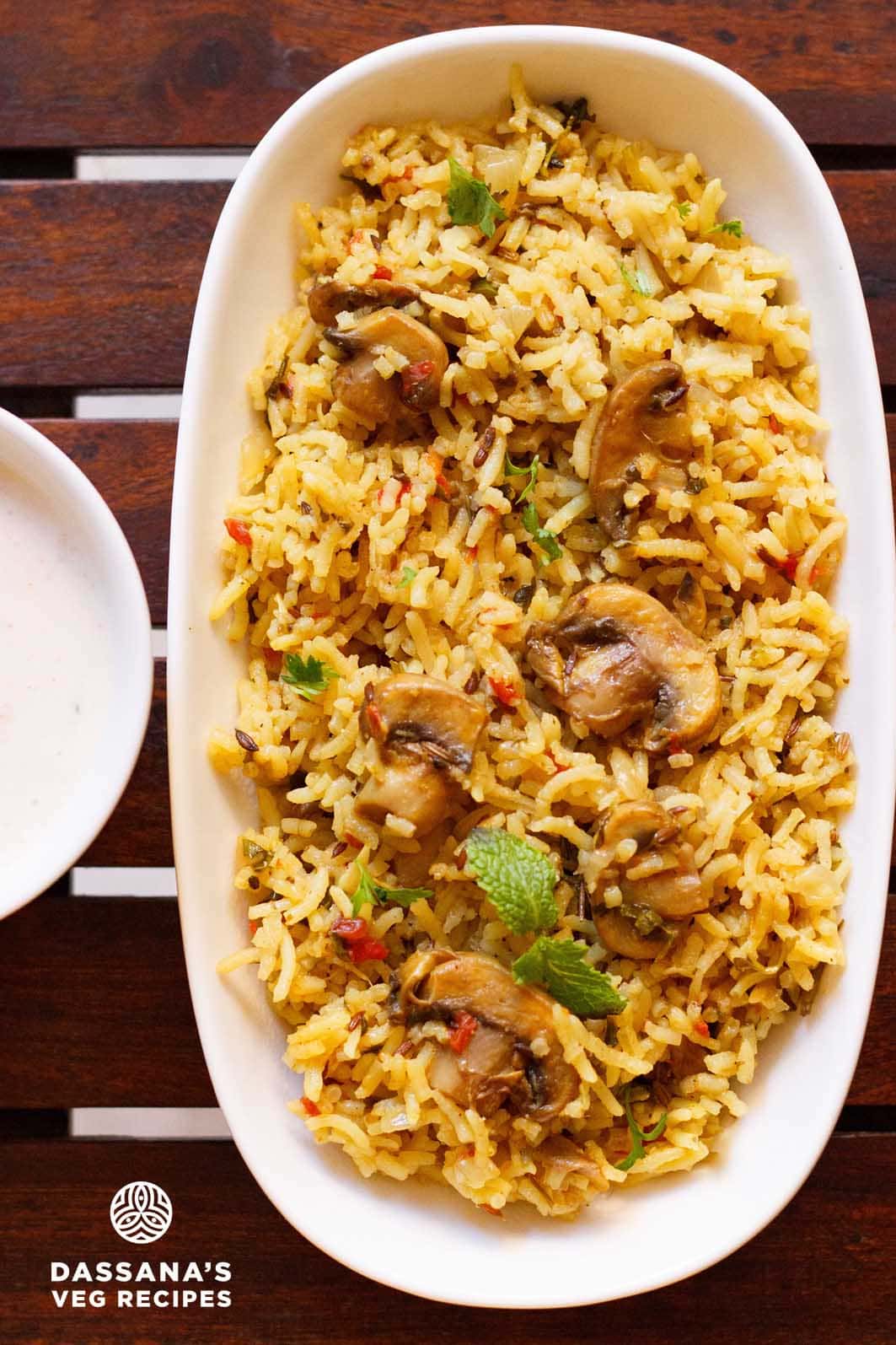 overhead shot of mushroom biryani in an oblong white tray on a wooden board.