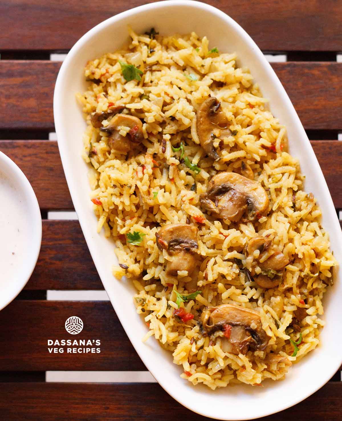 overhead shot of mushroom biryani in an oblong white tray on a wooden board.