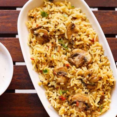 overhead shot of mushroom biryani in an oblong white tray on a wooden board.