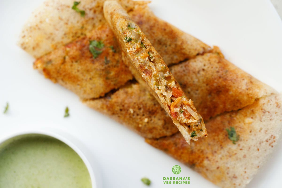 cross section image of paneer dosa with the paneer stuffing seen on a white plate with green coconut chutney with text layovers.