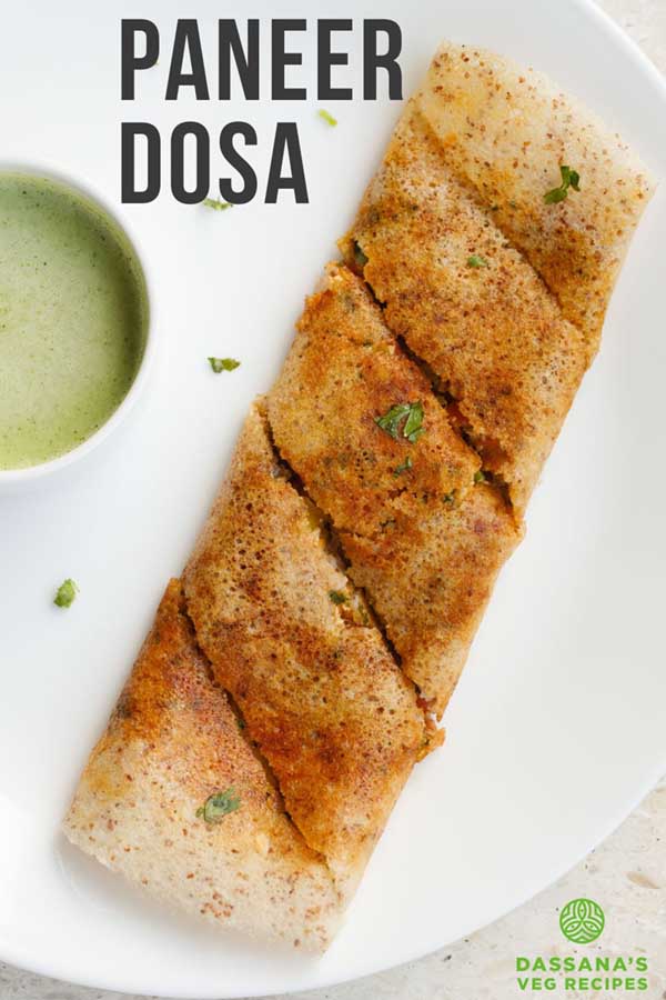 folded paneer dosa garnished with a few coriander leaves alongside a bowl of green colored coconut chutney.