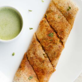 folded paneer dosa garnished with a few coriander leaves alongside a bowl of green colored coconut chutney.