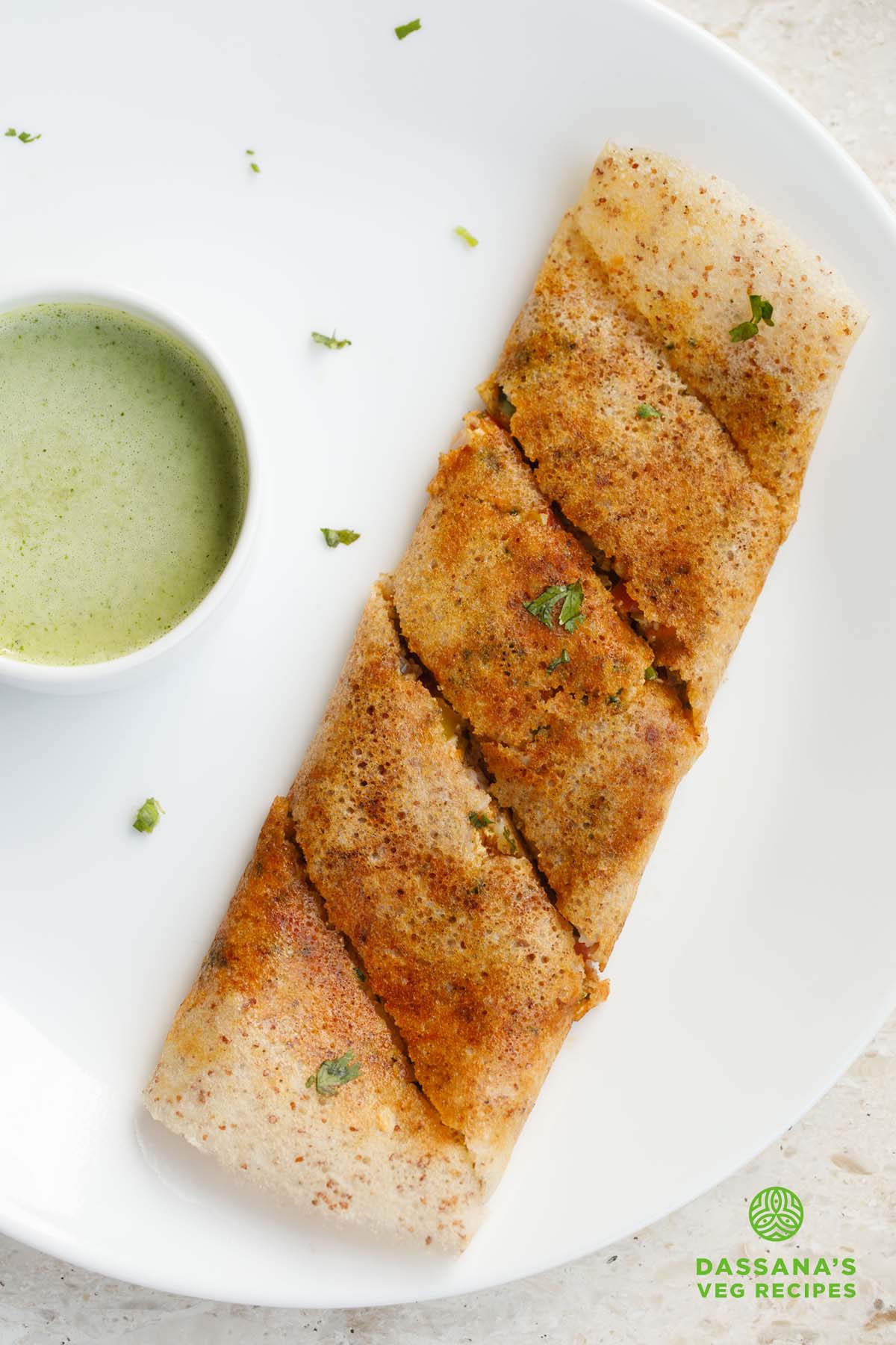 folded paneer dosa garnished with a few coriander leaves alongside a bowl of green colored coconut chutney.