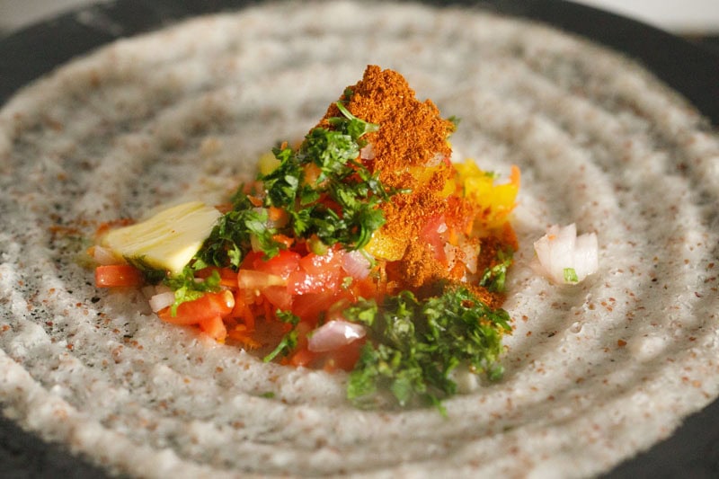 mound of ground spices, seasonings, coriander leaves, butter and green chillies on dosa covering the vegetables.