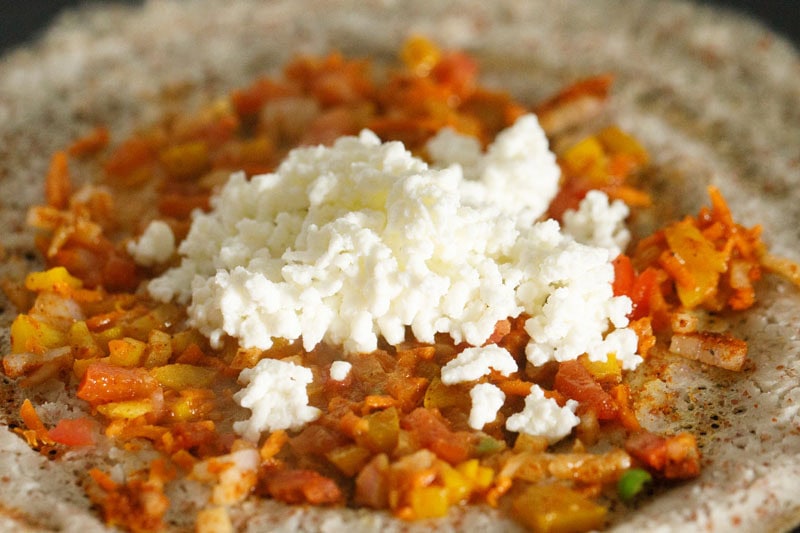 grated paneer on the layer of vegetables on dosa.