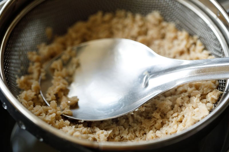 a spoon pressing the soya granules in strainer to remove extra water.