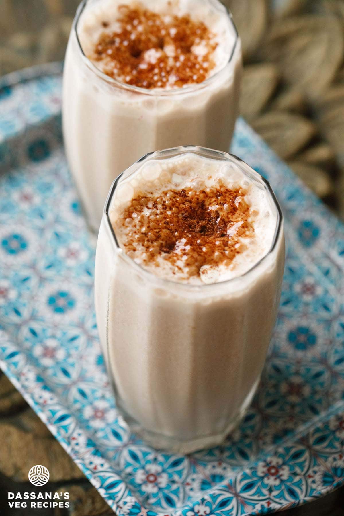 sharjah shake in 2 glasses sprinkled with bournvita on a blue design tray.