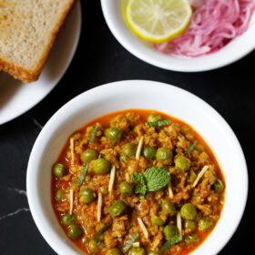 soya keema in a white bowl with bread and sliced onions, cucumber and lemon slice.