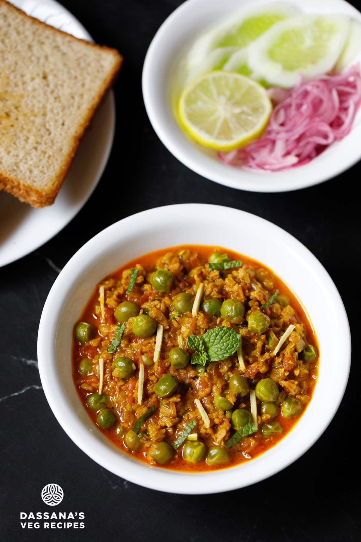 soya keema in a white bowl with bread and sliced onions, cucumber and lemon slice.