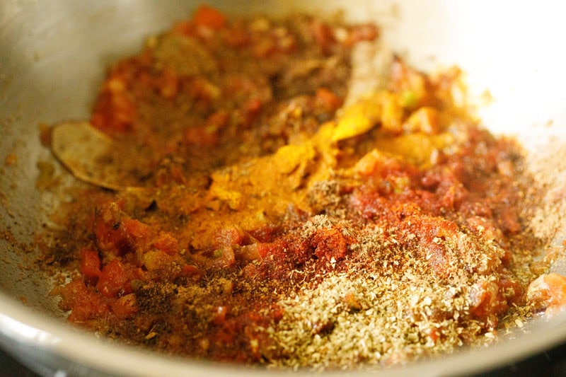 mix of various ground spices on the softened tomatoes in pan.