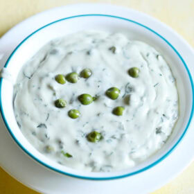 methi matar malai in a white bowl with a light blue rim, garnished with a few peas.