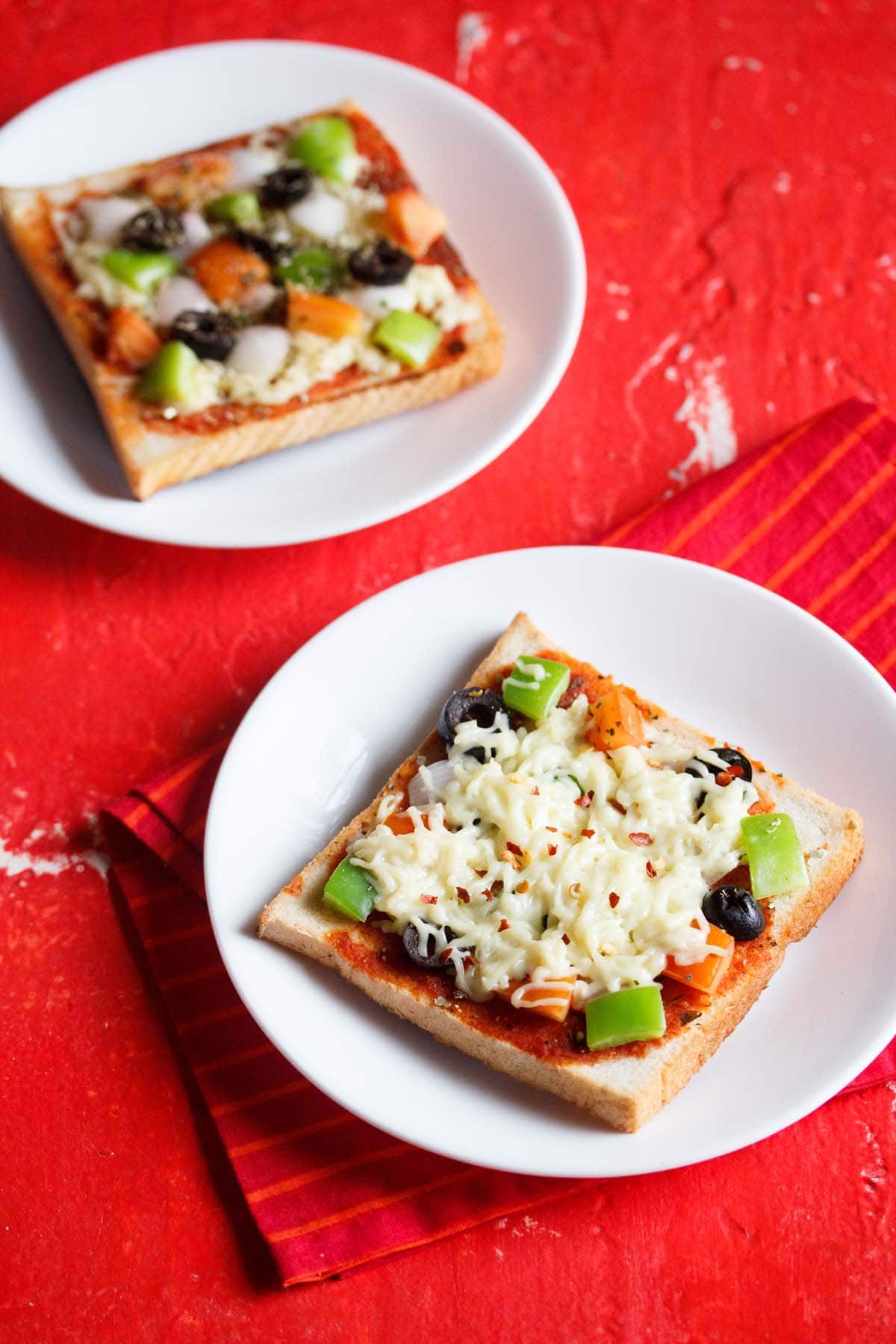 two white serving dishes, each with a slice of bread pizza on a red table with a red cloth underneath.